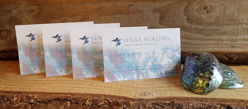 Gedrukte Sensa Healing cadeaubonnen voor massage en coaching, gepresenteerd op een houten plank met schelp